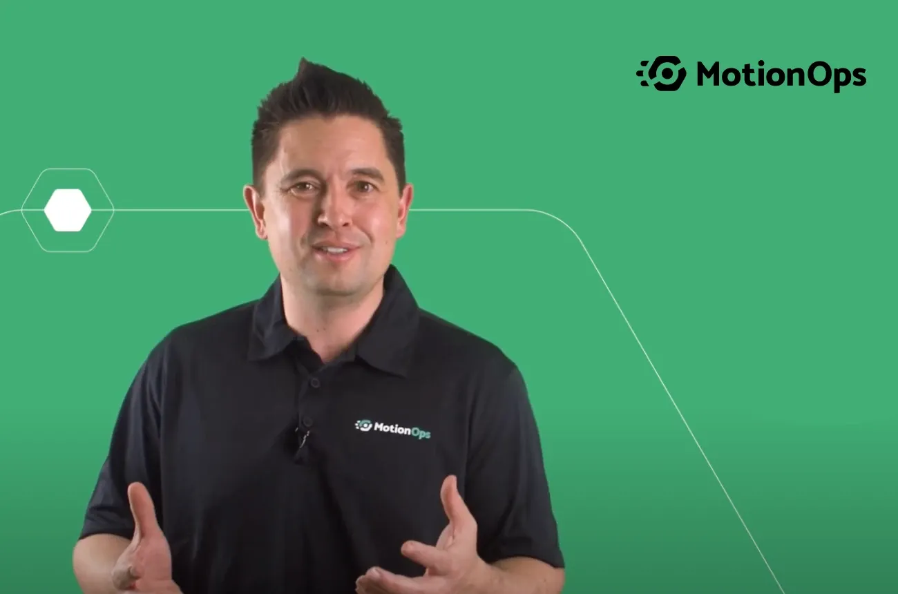A man in a black MotionOps polo shirt talks to the camera in front of a green background with the MotionOps logo