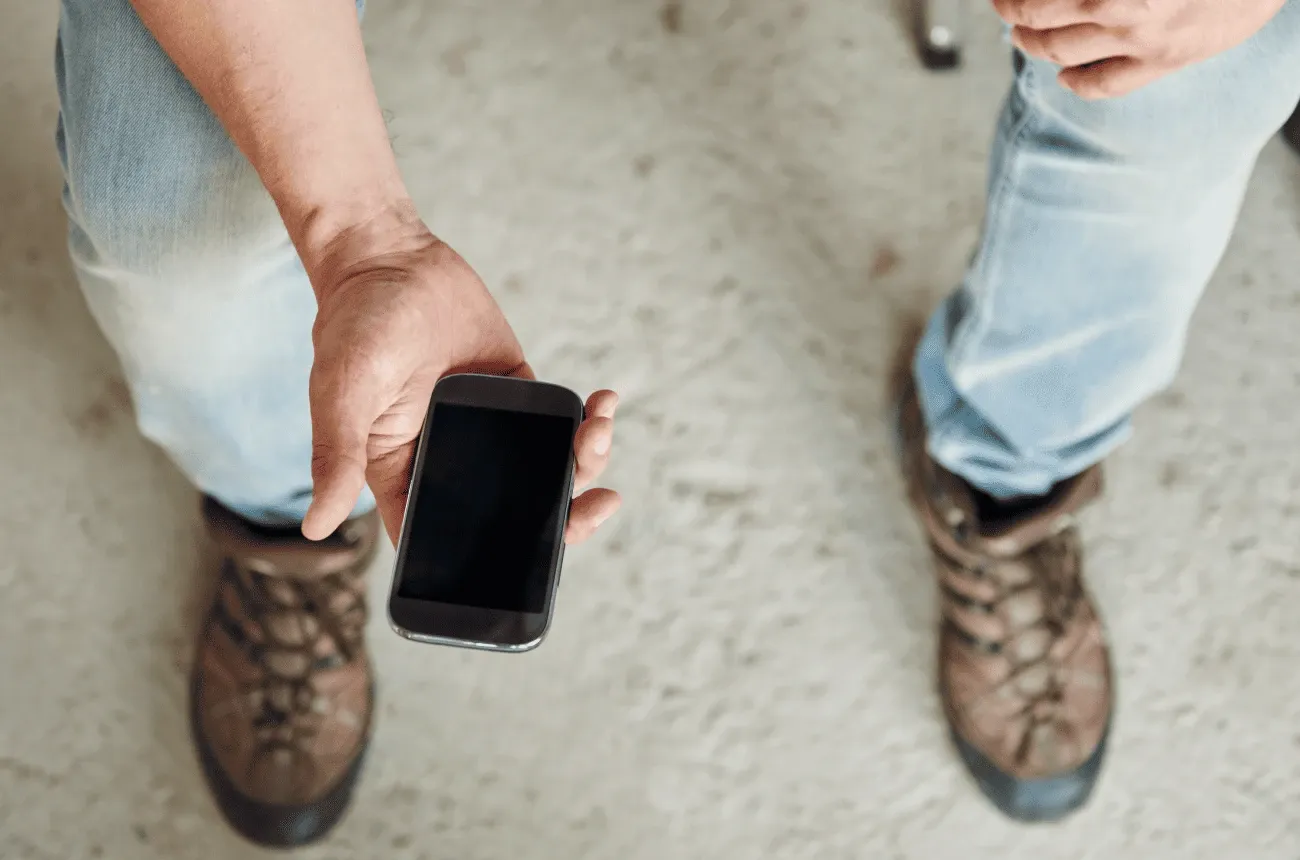 Overhead view of a person in jeans and work boots holding a smartphone with a blank screen
