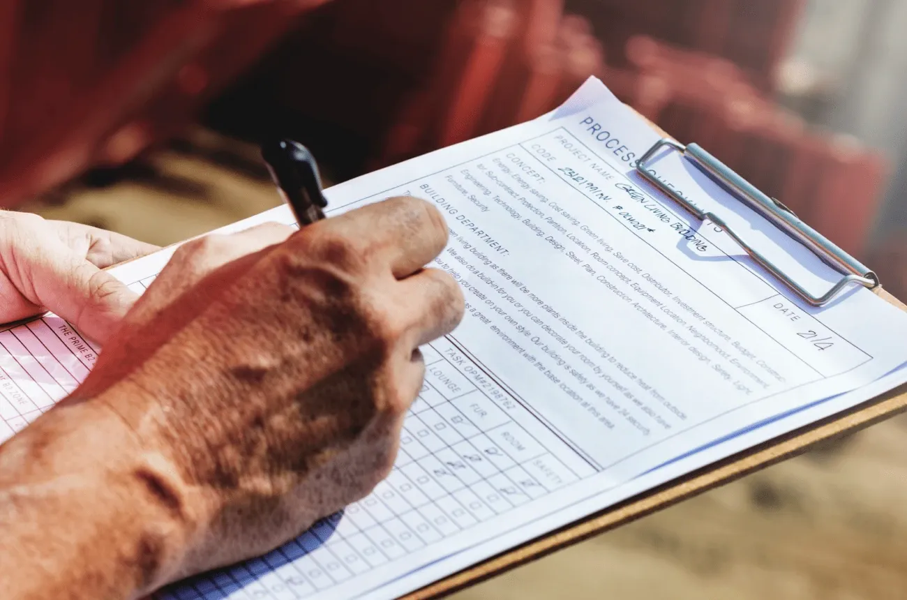 A hand writes on a construction checklist form clipped to a clipboard