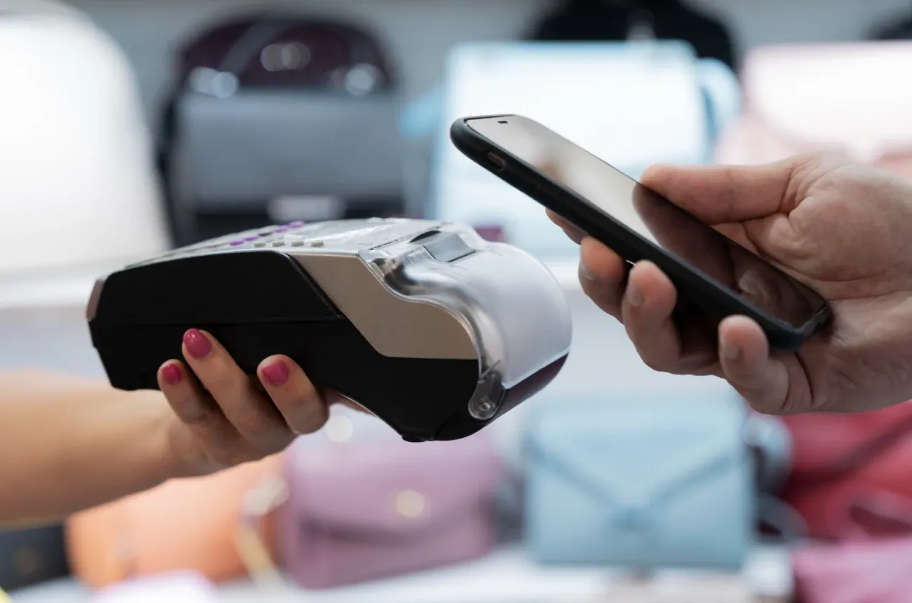 A customer holds a smartphone near a card payment terminal held by a cashier in a store